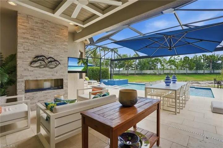 Covered outdoor living area featuring a stacked stone fireplace with a television, a ceiling fan, and recessed lighting