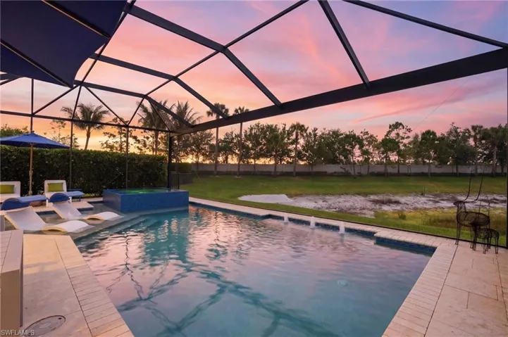 Screened pool enclosure featuring a rectangular pool, integrated spa with blue tile, and a spacious paver deck