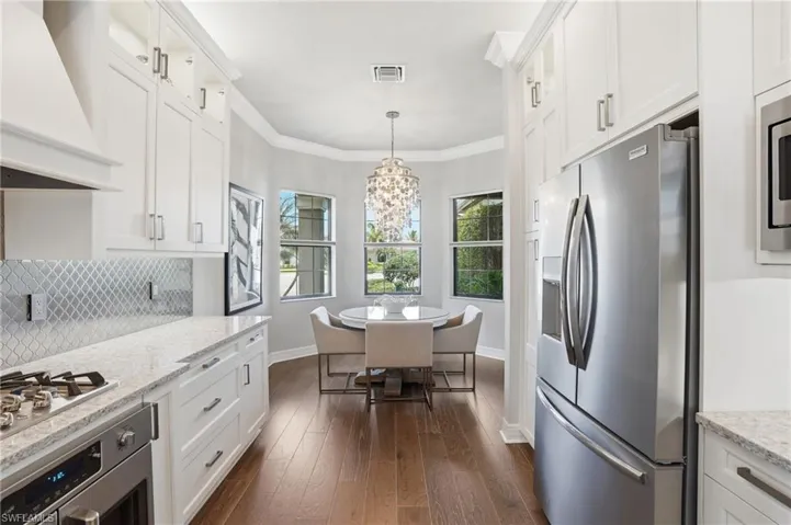 Modern kitchen featuring white cabinetry, stainless steel appliances, wood-finish flooring, light-toned countertops, and a decorative tile backsplash