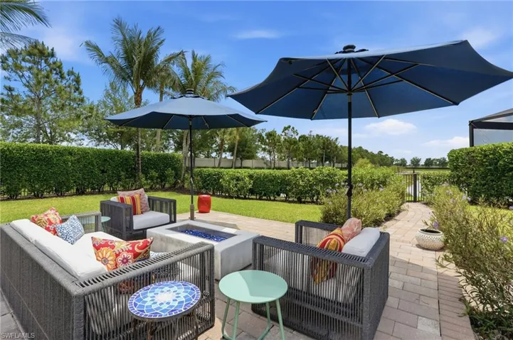 Patio area featuring paver flooring, a built-in fire pit, manicured hedges, and mature palm trees