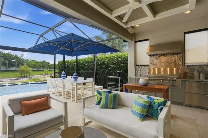 Screened outdoor living area with a built-in outdoor kitchen, stainless steel appliances, and a polished stone backsplash