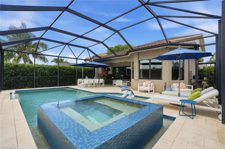 Screened outdoor living area featuring a rectangular pool and integrated spa with blue mosaic tile