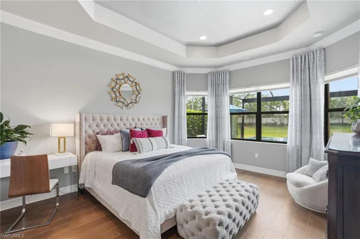 Room featuring a tray ceiling with recessed lighting, wood-finish flooring, and multiple windows with sheer and blackout blinds