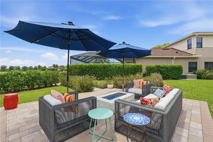Expansive outdoor living area featuring a brick paver patio, integrated fire pit, and mature perimeter landscaping