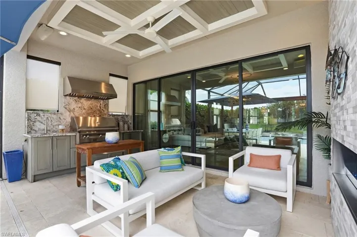 Covered outdoor living space featuring a coffered ceiling with a ceiling fan, a built-in outdoor kitchen with a stainless steel grill and hood, and sliding glass doors