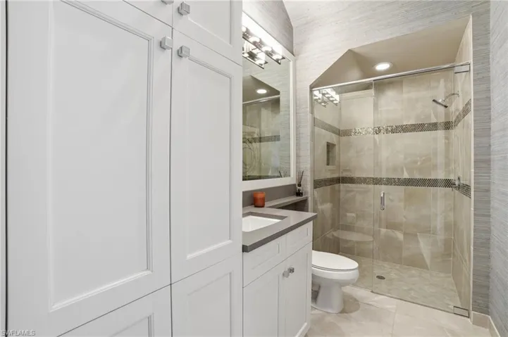 Modern bathroom featuring a custom built-in white cabinetry system, a single vanity with an undermount sink and gray countertop, a glass-enclosed shower with tiled walls, and recessed lighting