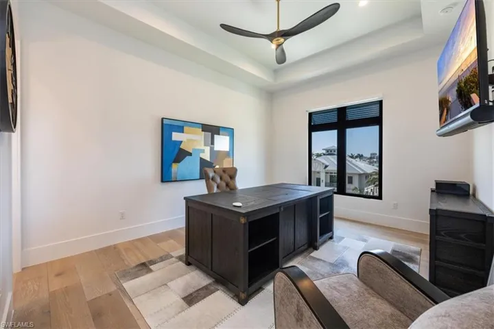 Office space with light wood-type flooring, a raised ceiling, ceiling fan, and baseboards