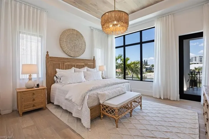 Bedroom with baseboards, light wood-type flooring, a raised ceiling, and a chandelier
