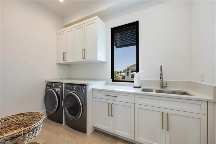 Clothes washing area featuring separate washer and dryer, a sink, cabinet space, and light wood finished floors