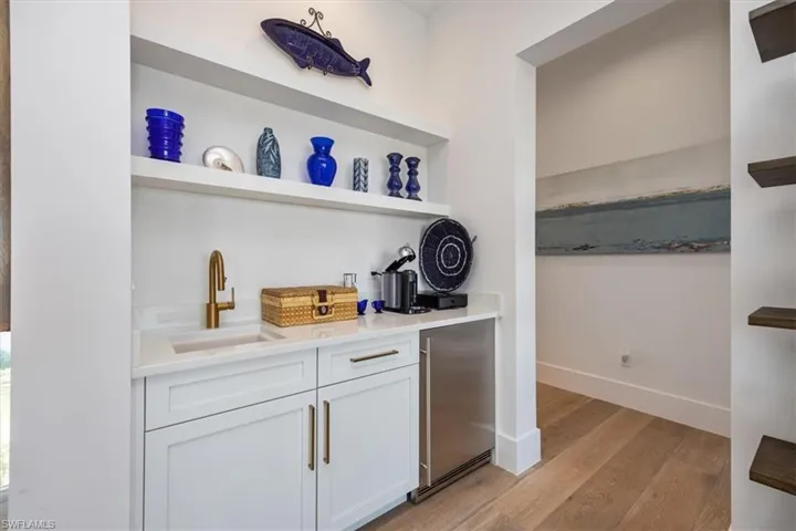 Bar featuring wet bar, high end refrigerator, baseboards, a sink, and light wood finished floors