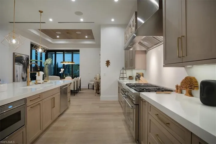 Kitchen with wall chimney range hood, a sink, light wood-style floors, light countertops, and stainless steel appliances