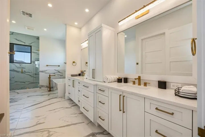 Bathroom with double vanity, a freestanding bath, a sink, a marble finish shower, and recessed lighting