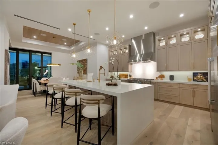Kitchen with a large island with sink, light wood-type flooring, light countertops, a breakfast bar, and wall chimney exhaust hood