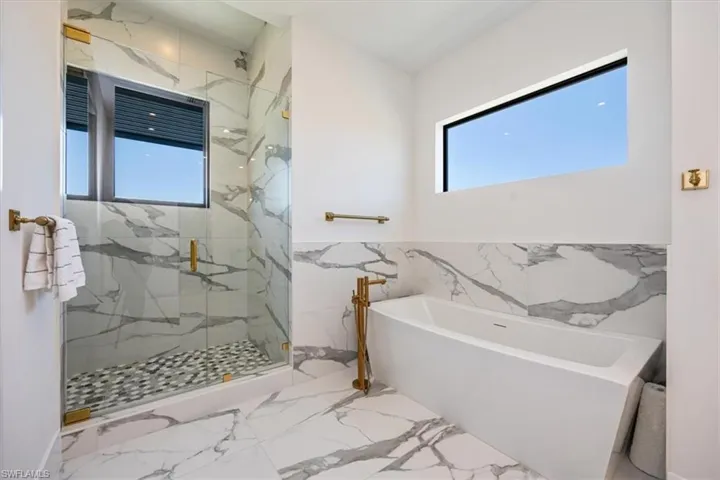 Bathroom with marble finish floor, a freestanding tub, a marble finish shower, and tile walls