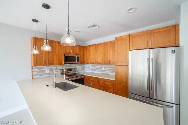 Kitchen with stainless steel appliances, tasteful backsplash, hanging light fixtures, a peninsula, and recessed lighting