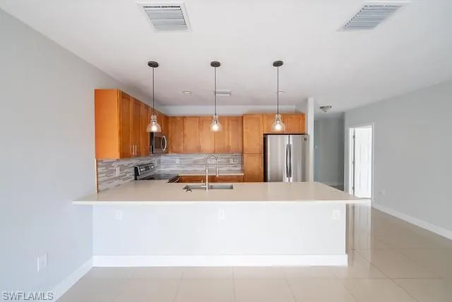 Kitchen featuring decorative backsplash, appliances with stainless steel finishes, pendant lighting, and a peninsula