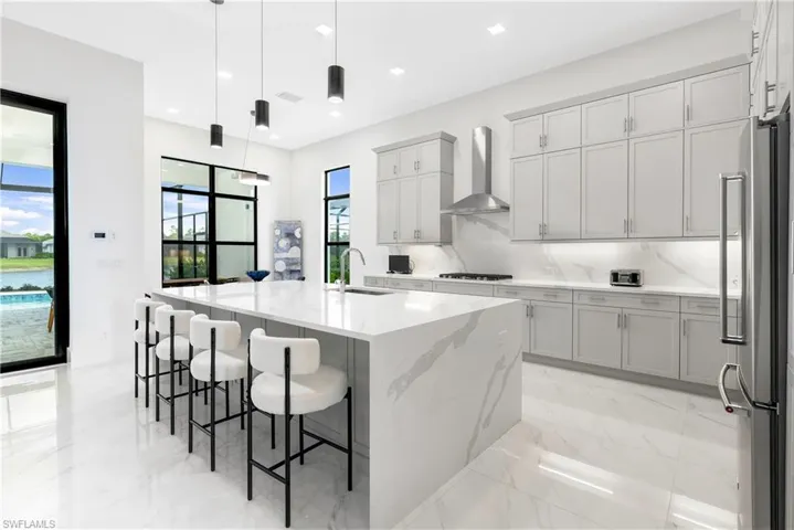 Kitchen with decorative light fixtures, light stone countertops, an island with sink, light marble finish flooring, and a breakfast bar