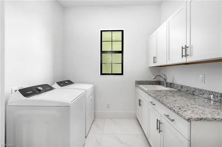 Washroom with light marble finish flooring, cabinet space, and washing machine and clothes dryer