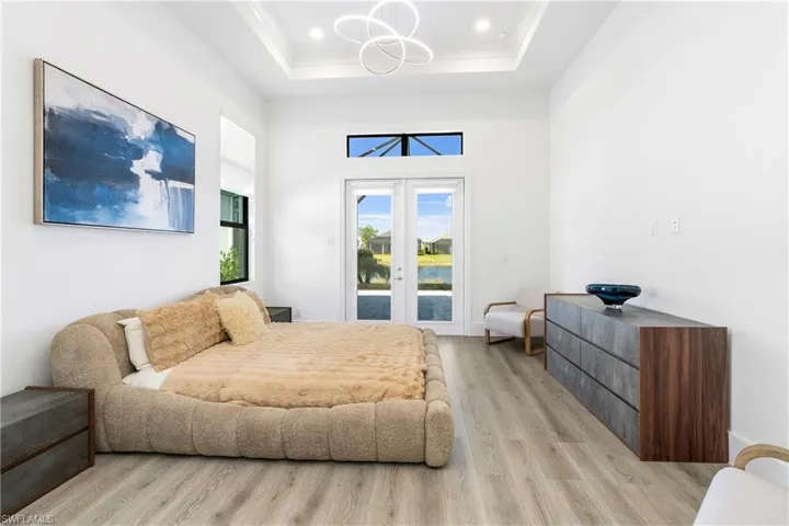 Bedroom with access to exterior, light wood finished floors, french doors, a high ceiling, and a chandelier