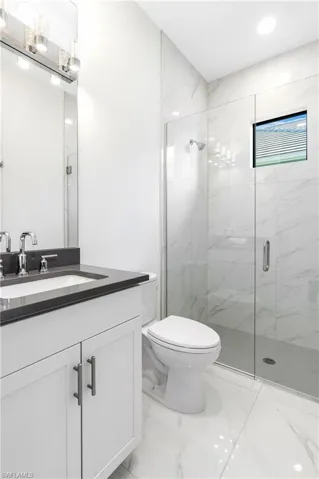 Bathroom with light marble finish floors, vanity, a marble finish shower, and recessed lighting