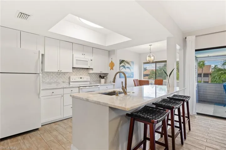 Kitchen with white appliances, decorative backsplash, white cabinetry, and light wood-type flooring