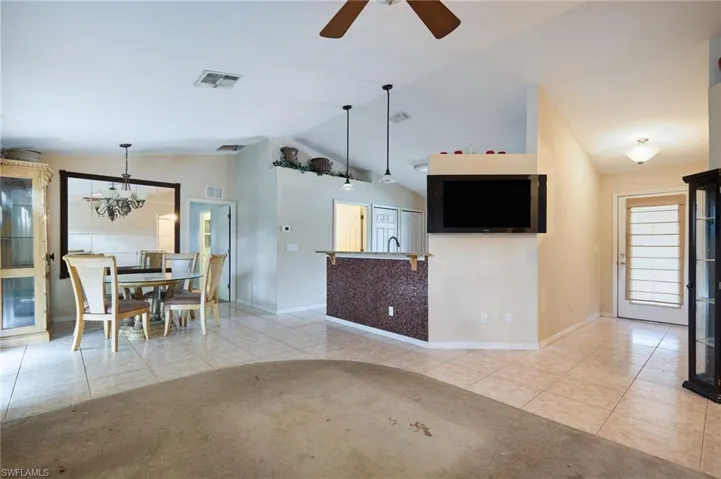 Unfurnished living room with ceiling fan with notable chandelier, lofted ceiling, light tile patterned flooring, and sink