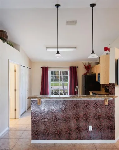 Kitchen with kitchen peninsula, hanging light fixtures, black appliances, light tile patterned floors, and light brown cabinetry