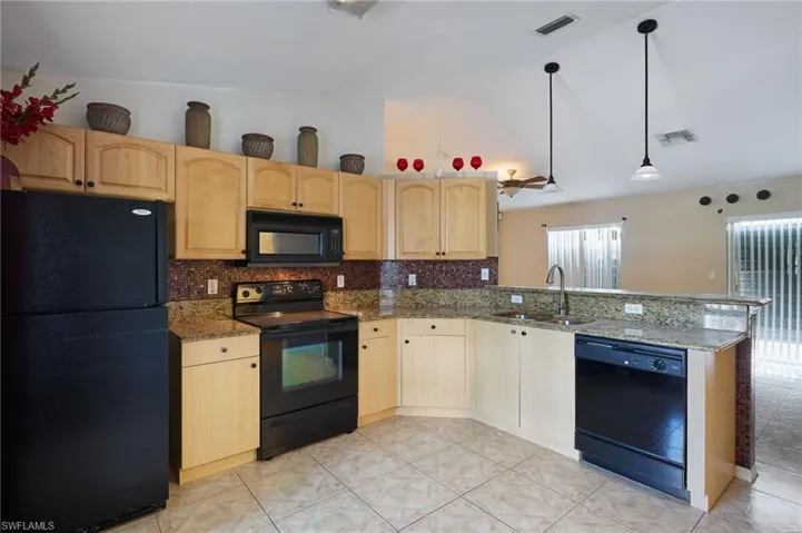 Kitchen with black appliances, light brown cabinets, decorative light fixtures, and sink