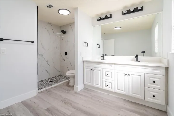 Bathroom featuring tiled shower, wood-type flooring, toilet, and vanity