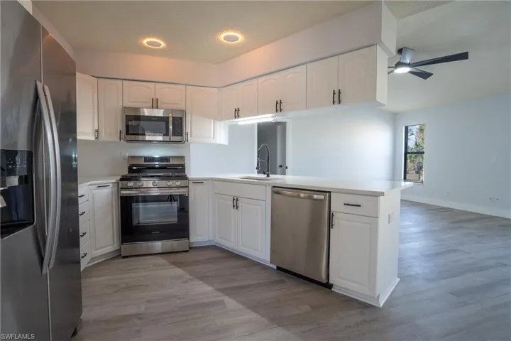 Kitchen featuring sink, stainless steel appliances, light hardwood / wood-style floors, white cabinets, and kitchen peninsula