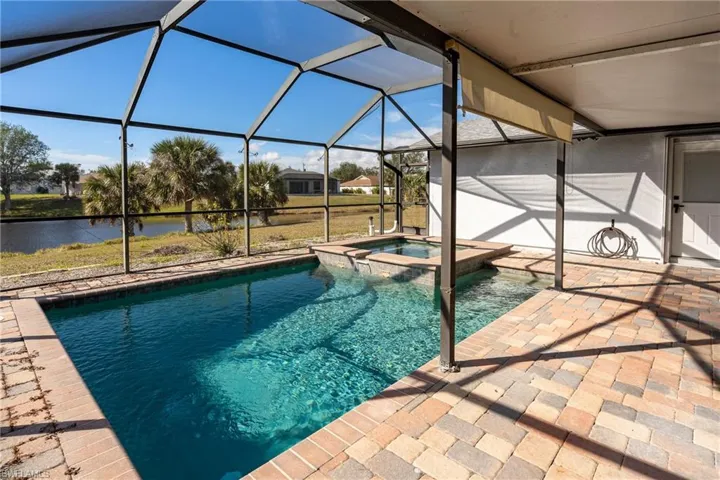 View of pool with a patio area, a water view, glass enclosure, and an in ground hot tub