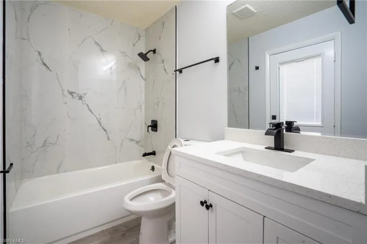 Full bathroom featuring vanity, wood-type flooring, a textured ceiling, tiled shower / bath, and toilet