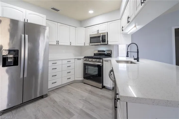 Kitchen featuring appliances with stainless steel finishes, kitchen peninsula, sink, and white cabinets