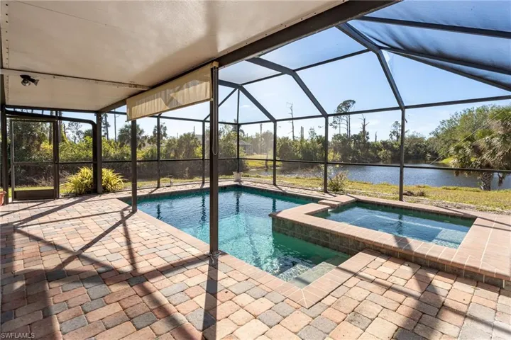 View of pool with an in ground hot tub, a water view, screened enclosure, and a patio area