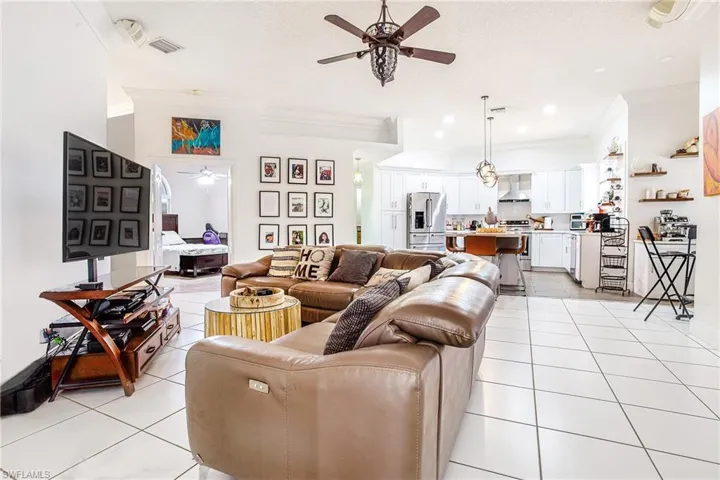 Living room with ceiling fan, ornamental molding, light tile patterned flooring, and a textured ceiling