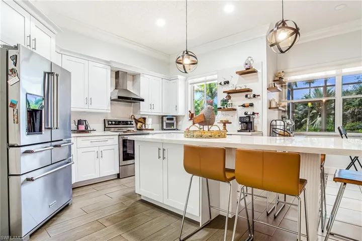 Kitchen featuring stainless steel appliances, white cabinetry, a breakfast bar area, pendant lighting, and ornamental molding