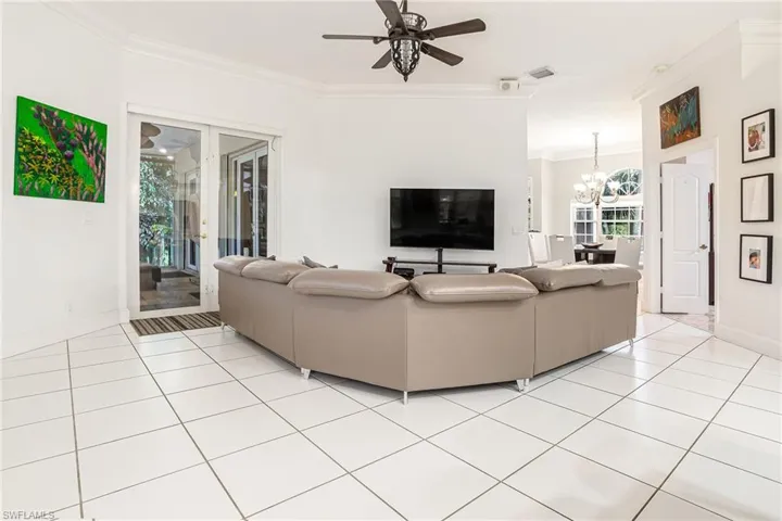 Living area with ornamental molding, ceiling fan, a chandelier, light tile patterned flooring, and french doors