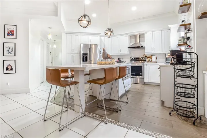 Kitchen with a kitchen breakfast bar, stainless steel appliances, ornamental molding, wall chimney range hood, and a kitchen island