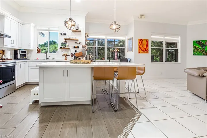 Kitchen with crown molding, white cabinetry, a kitchen bar, decorative light fixtures, and stainless steel electric stove