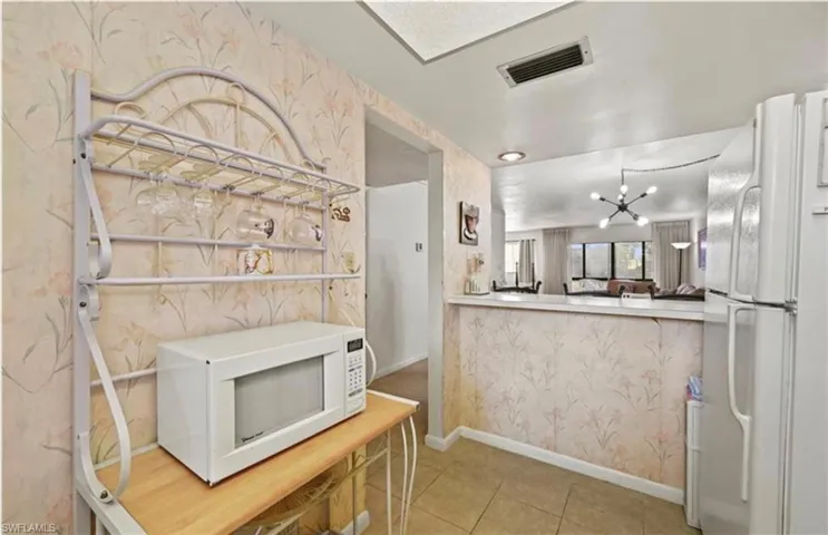 Kitchen with white appliances, wallpapered walls, a chandelier, light tile patterned floors, and light countertops