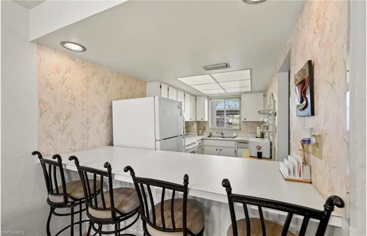 Kitchen with wallpapered walls, light countertops, freestanding refrigerator, white cabinets, and a breakfast bar area