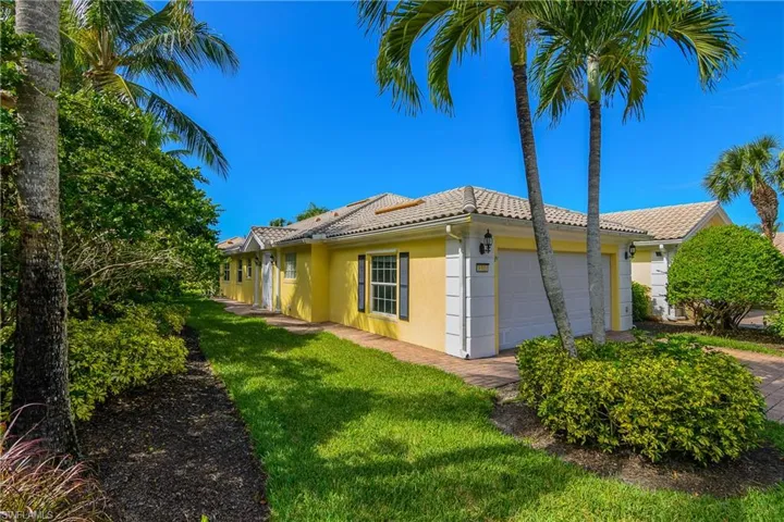 Stucco exterior featuring a tiled roof, multi-pane windows with decorative shutters, a paved driveway, and established palm tree landscaping
