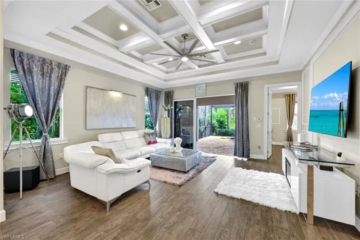 Living room featuring coffered ceiling, crown molding, baseboards, visible vents, and wood finished floors