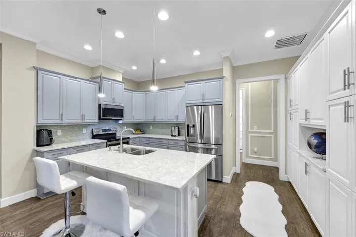 Kitchen featuring decorative light fixtures, stainless steel appliances, a center island with sink, dark wood-style floors, and visible vents