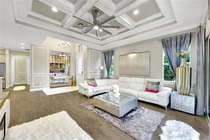 Living area with ornamental molding, ceiling fan with notable chandelier, beamed ceiling, and coffered ceiling