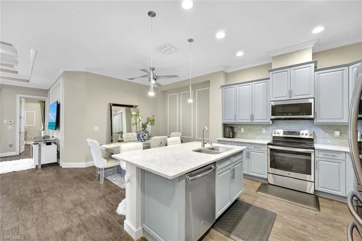 Kitchen with stainless steel appliances, tasteful backsplash, an island with sink, a sink, and gray cabinets