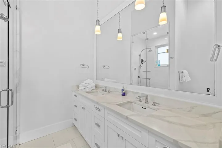 Bathroom featuring double vanity, light tile patterned floors, and a stall shower