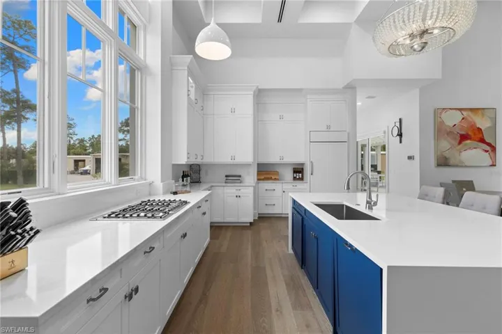 Kitchen with white cabinetry, light stone counters, dark wood-style flooring, a center island with sink, and hanging light fixtures