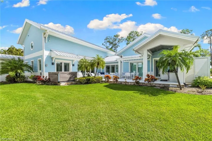 Rear view of property with a hot tub, a lawn, and a patio