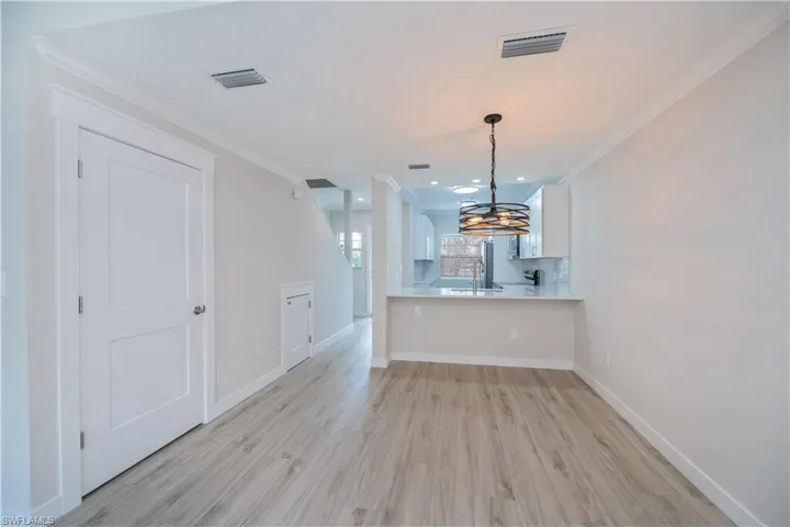 Kitchen with light countertops, ornamental molding, light wood-type flooring, hanging light fixtures, and white cabinetry